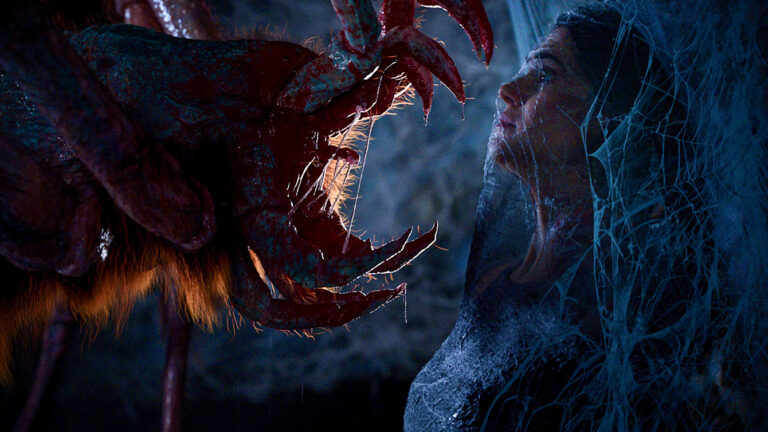 Don't Move trailer prehistoric spider approaches a victim trapped in webbing
