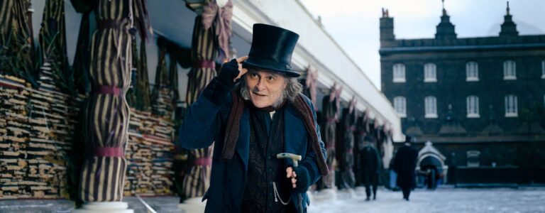 Johnny Depp as Ebenezer Scrooge tips his top hat in a snowy Victorian market in Ebenezer.